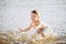 Boy child playing makes splashes, beats hands on the water in the river at sunset