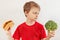 Boy chooses between hamburger and vegetable on white background