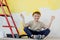 A boy in a construction uniform sits near paint paints. Repairs. Painting the walls