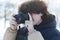 A boy with curly long hair takes a picture with a DSLR camera. Winter photo shoot outdoors