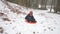 A boy in dark overalls is spinning on a sled down in the woods