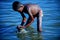 The boy didn`t wear a shirt in the Ganga River. He bent and used his hand to search for valuable