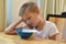 Boy doesn`t want to eat. Unhappy child at the kitchen table. Tasteless food.