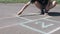 Boy is drawing hopscotch on the asphalt.