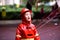 Boy dressed as a fireman with red raincoat splashes on the grass of a park a rainy day