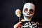 Boy dressed as a skeleton holding a skull lollipop in his hand on the black background