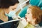 Boy drills the tooth of female dentist. Little child on dental chair.