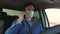 Boy is driving and talking on android. Healthy young guy in protective sterile medical mask drives a car. Free man with