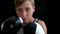 The boy is engaged in boxing. In the foreground there are hands in black and white gloves, the boy`s face is blurry. A