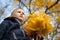 A boy of European appearance with a bouquet of leaves. Yellow blurred background. Bottom view. Autumn day