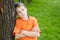 Boy with folded arms, standing leaned to tree