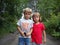 A boy and a girl are brother and sister. Children with blond hair walk next to trees and bushes. Girl with glasses and a red t-