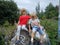 A boy and a girl are brother and sister. Children with blond hair walk next to trees and bushes. Girl with glasses and a red t-