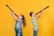 A boy and a girl with clarinets are standing with their backs to each other, playing the clarinet, on a yellow background