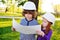 Boy and girl in construction helmets looking at white sheet of paper or drawing and smiling