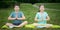 Boy and girl doing yoga, outdoors, on a background of green grass, sitting on a gymnastic mat