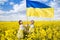 Boy and girl hold yellow-blue flag, stand among flowering yellow rapeseed field