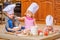 Boy and girl and a newborn kid with them in chef`s hats sitting on the kitchen floor soiled with flour