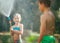 Boy and girl playing in garden, pouring with water each other from the hose, making a rain. Happy childhood concept image