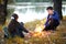 Boy and girl sitting on the river Bank, make a fire, autumn forest at sunset, beautiful nature and reflection of trees in the wate