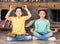 Boy and girl with tablets on heads sitting in lotus pose in library