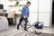 The boy in glasses and a blue shirt is cleaning the flat. Vacuuming the apartment with a vacuum cleaner by a school-age boy.
