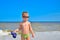 A boy in glasses stands on the beach by the sea