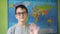 a boy with glasses waves his hand standing against the background of a political map of the world. a smile on the face