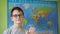 a boy with glasses waves his hand standing against the background of a political map of the world. a smile on the face