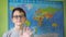 a boy with glasses waves his hand standing against the background of a political map of the world. a smile on the face
