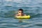 A boy in goggles learns to swim with a yellow inflatable mattress. Teenager in goggles swims in the sea with big splashes.