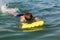 A boy in goggles learns to swim with a yellow inflatable mattress. Teenager swims in the sea with big splashes.
