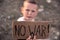 A boy with a grimy face and sad eyes holds a cardboard poster with the inscription NO WAR