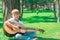 A boy with a guitar sits under a tree, sings songs and enjoys nature