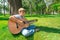A boy with a guitar sits under a tree, wide angle photo