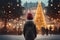 boy in a hat in the central square, looking at a large Christmas tree decorated for Christmas, rear view