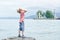 Boy in hat standing on the beach and looking up. Small lighthouse in the distance. Back view