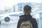 A boy in headphones with a backpack stands near the window at the airport and looks at the plane.