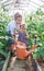 The boy helps the little sister to water green plants in a garden