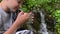 A boy hiker, trekker getting clear fresh water from a mountain spring in metal tourist cup and drinking