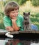 Boy and his beloved kitten playing with a boat from pier in pond summer evening