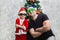 A boy and his dad in funny sunglasses and Santa hats are standing near the Christmas tree with their arms crossed on their chest.