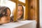 A boy with his mother curiously peeks out the window of a wooden house