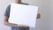 Boy holding in his hands blank empty white mock up board poster. Grey wall on background. Close up