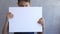 Boy holding in his hands blank empty white mock up board poster. Sad kid covering his face with canvas board. Grey wall