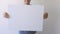 Boy holding in his hands and show blank empty white mock up board poster. Grey wall on background. Close up