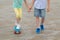 The boy holds the girls hand, teach skating on a sports Board, legs close-up, on the background of stone blocks