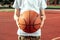 The boy holds in his hands a basketball closeup, against the background of a basketball court. The concept of a sports lifestyle,