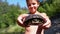 Boy Holds Turtle in Arms and Smiles on Background of River with Green Vegetation