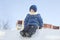 Boy In Hooded Jacket Sitting On Snow Heap